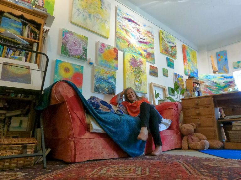 Artist Melody Hawtin in her studio surrounded by abstract art, flower paintings, landscape and seascape paintings